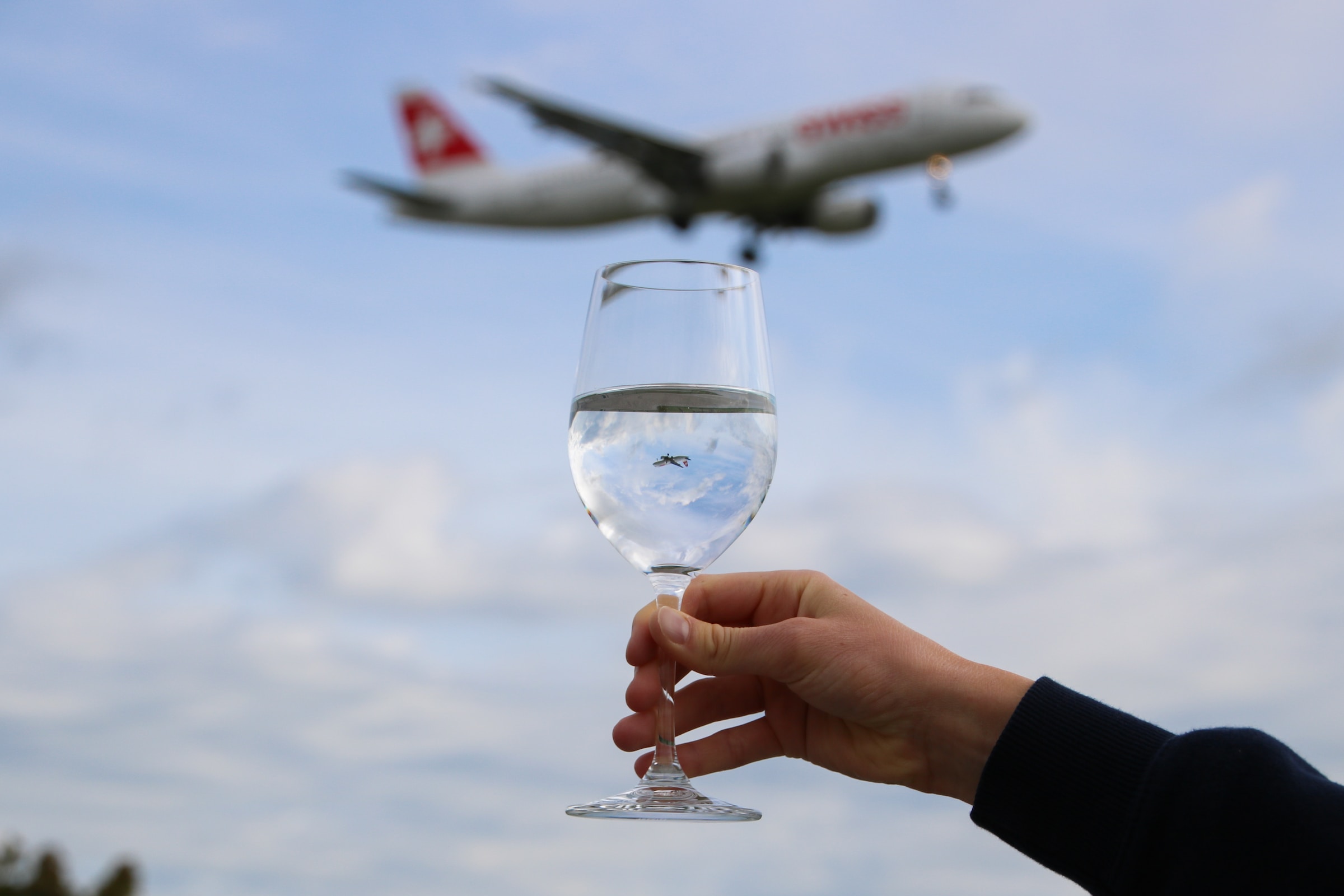 person holding clear wine glass with airplane in the sky