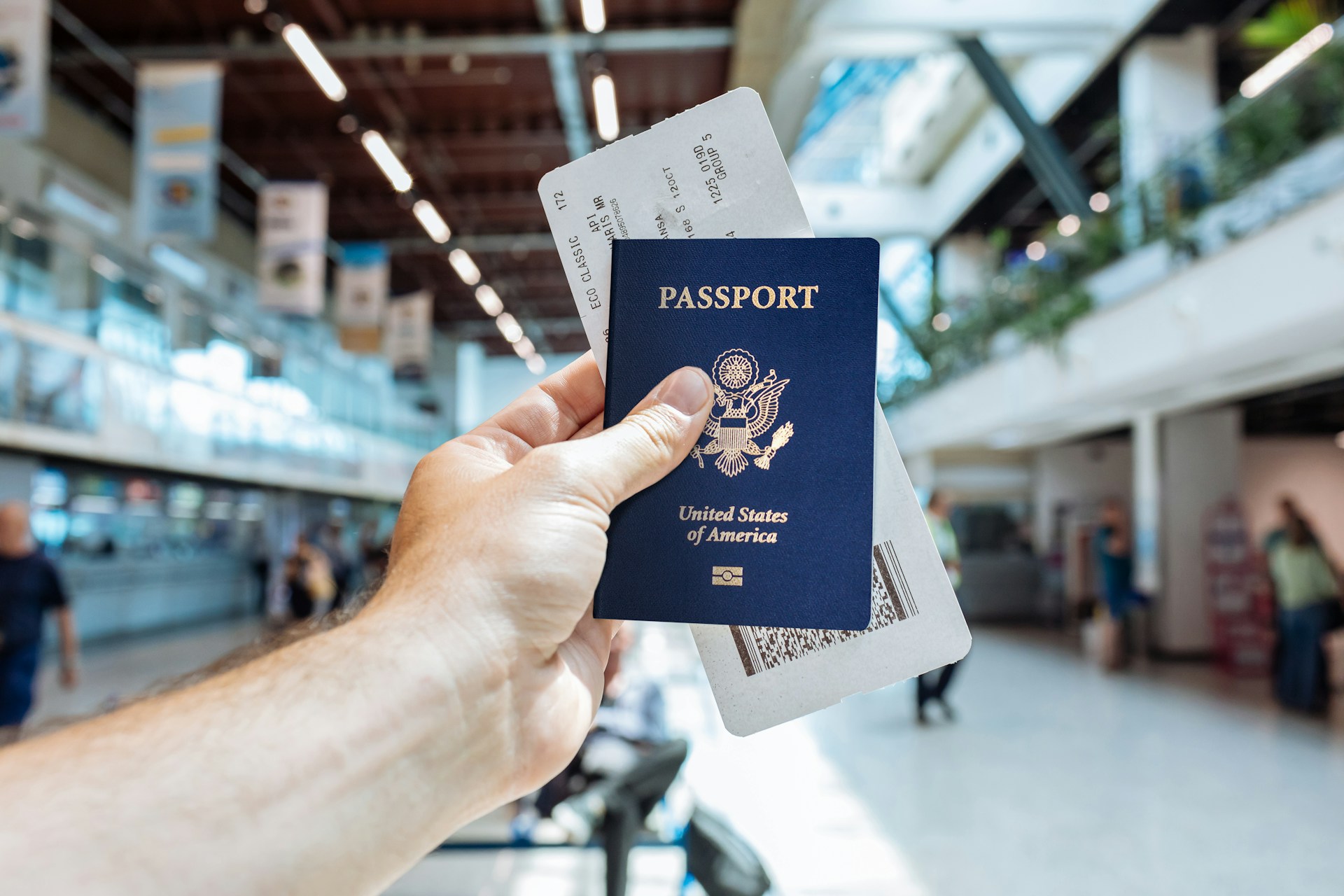 person holding up passport and boarding ticket in the middle of airport